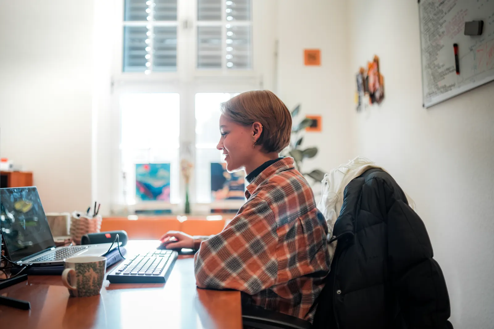 Eine Kollegin arbeitet lächelnd am Rechner im sorum-Büro, hinter ihr ein helles Fenster