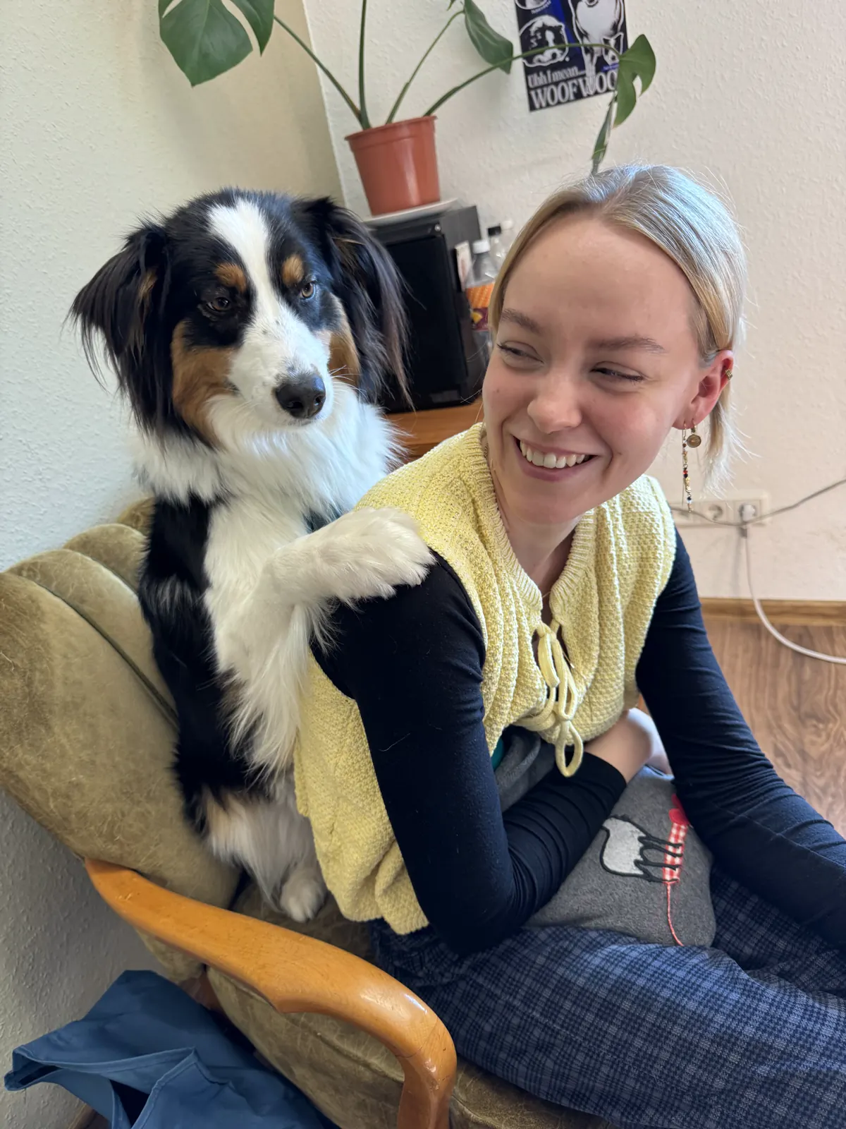 Eine Kollegin lacht, neben ihr sitzt der Bürohund und legt ihr die Pfote auf die Schulter